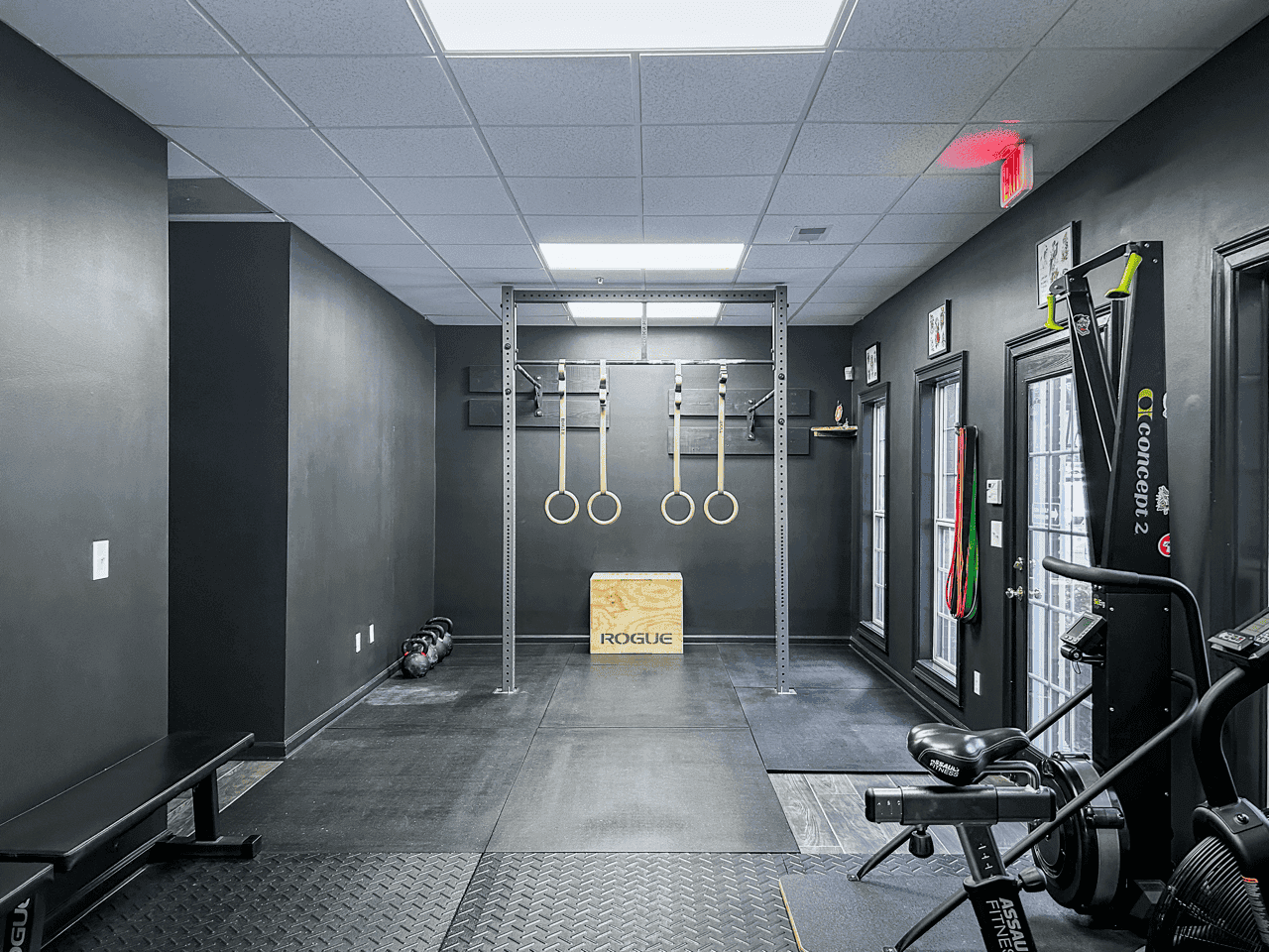 A squat rack with gymnastic rings and kettlebells at Hustle House Health & Wellness in Woodstock, GA