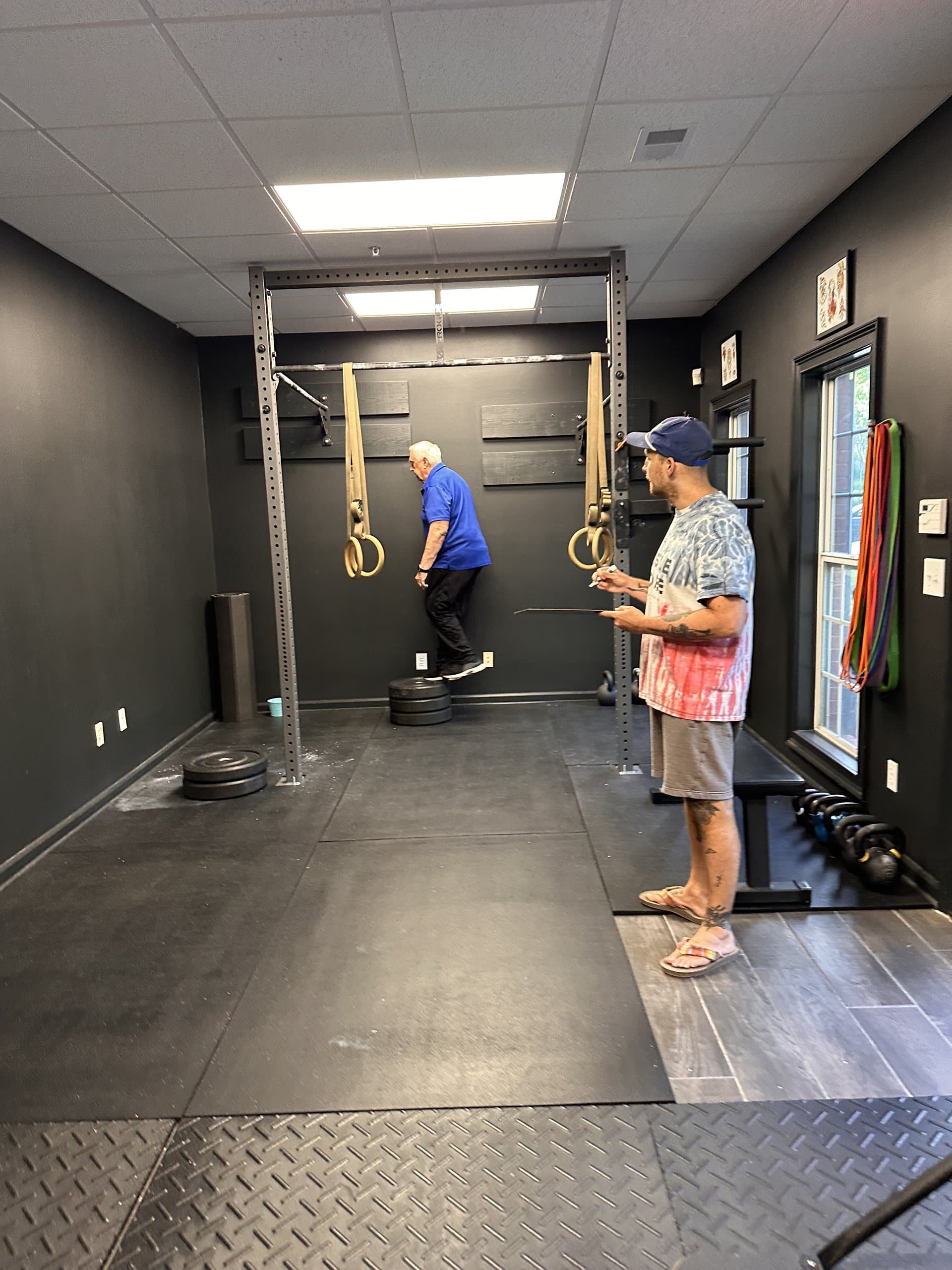 A coach assessing a member's gymnastic ring work at Hustle House Health & Wellness in Woodstock, GA