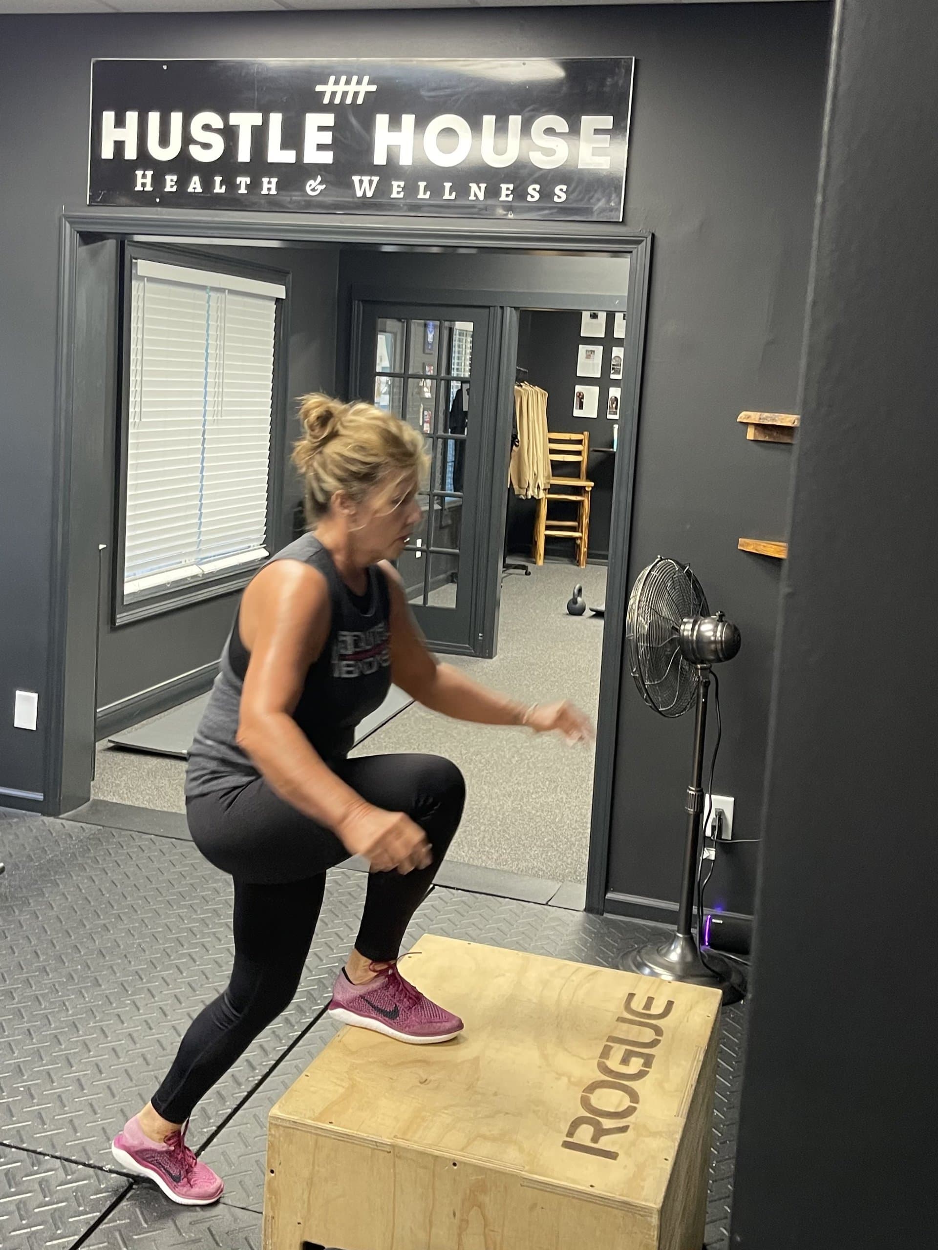 A member performing a box jump onto a wooden platform at Hustle House Health & Wellness in Woodstock, GA