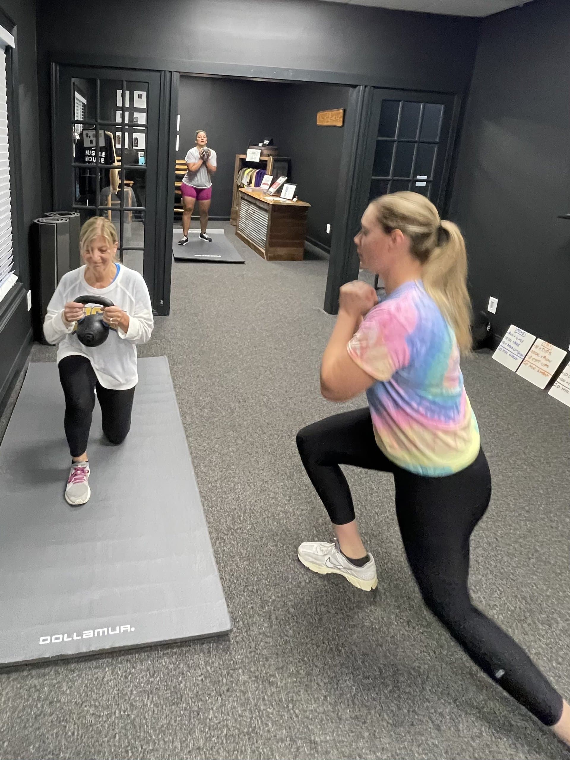 Members performing kneeling kettlebell lunges in a small group class at Hustle House Health & Wellness in Woodstock, GA