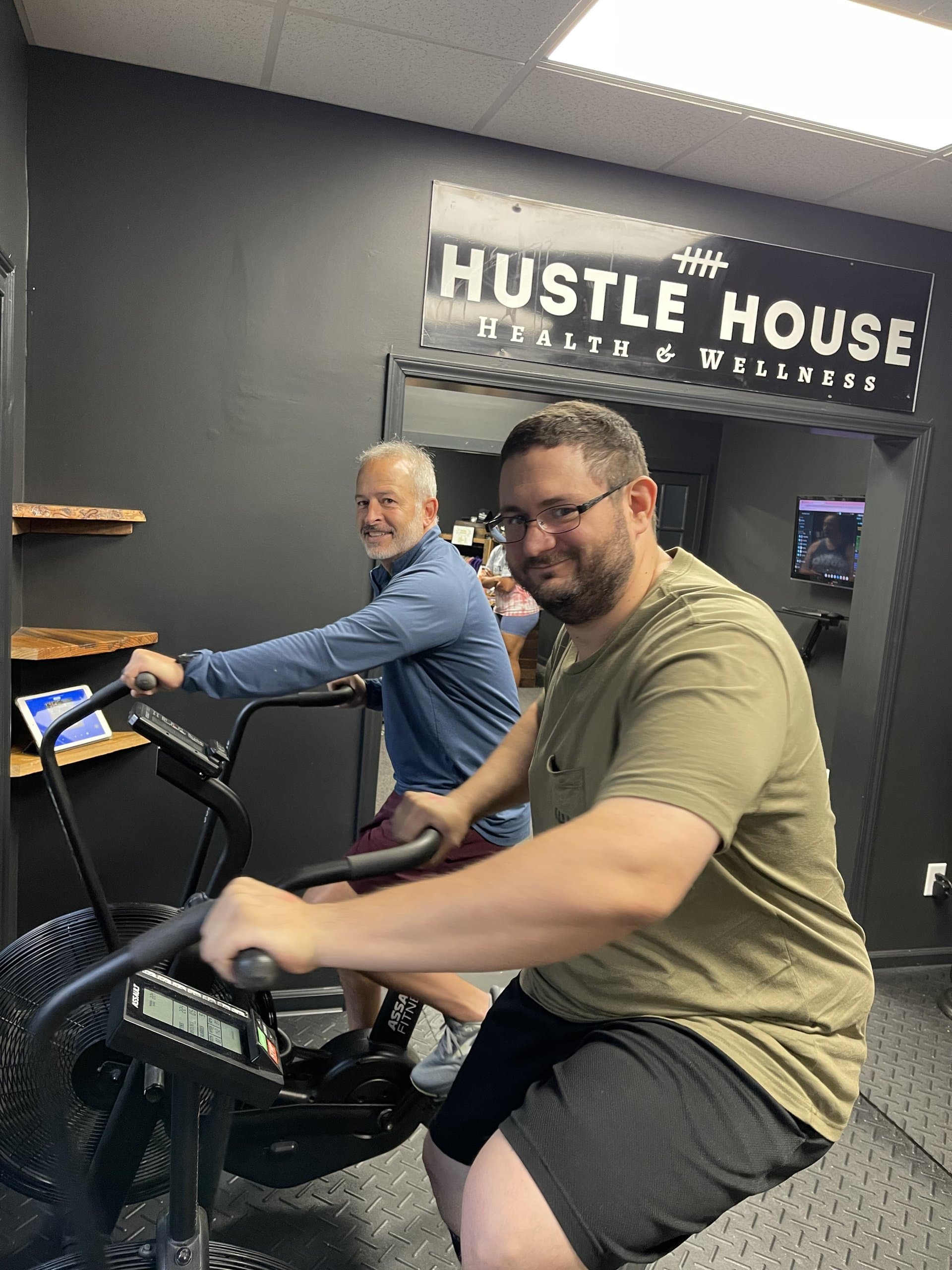 Two members riding air bikes for conditioning work at Hustle House Health & Wellness in Woodstock, GA