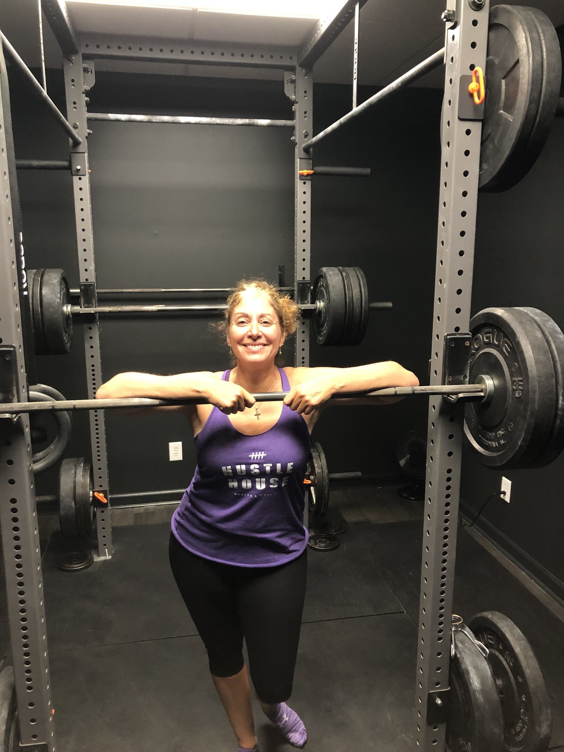 A member resting on a loaded barbell in the squat rack at Hustle House Health & Wellness in Woodstock, GA