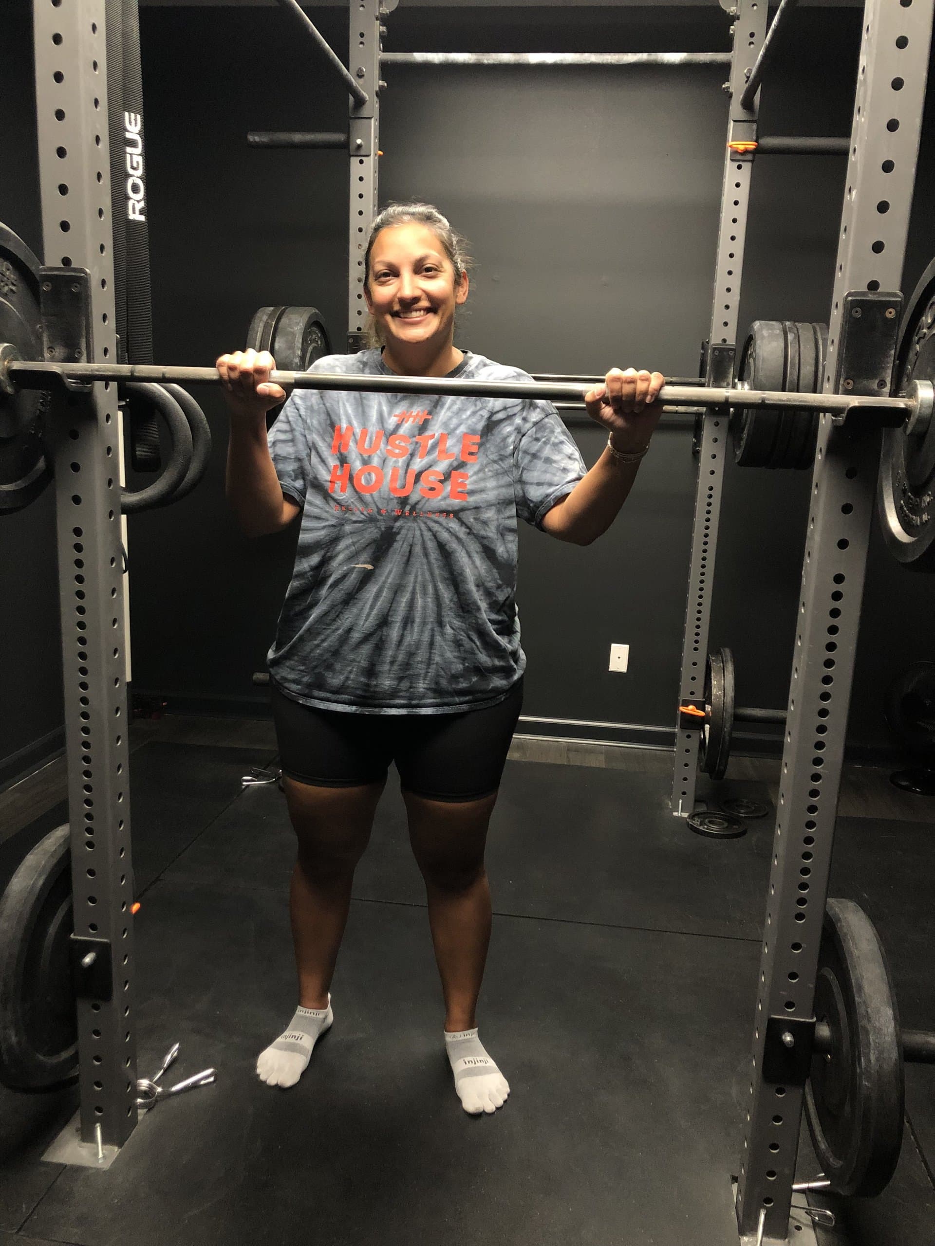 A member holding a loaded barbell in the squat rack at Hustle House Health & Wellness in Woodstock, GA
